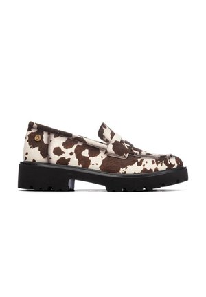 Zapato tipo mocasín con suela negra gruesa y parte superior con patrón de piel de vaca marrón y blanca sobre fondo blanco.