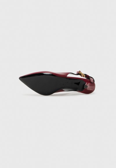 Red patent leather high heel shoe with a pointed toe, ankle strap, and gold hardware accent. Features a contrasting black sole.