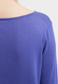 Niebieski sweter z dzianiny o szerokim dekolcie i rękawach raglanowych, ukazujący miękką teksturę i staranne wykończenie, z naciskiem na jednolity kolor bez wzorów.