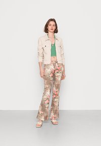 Calças castanhas com padrão floral e impressão de leopardo, combinadas com um top verde cropped e uma jaqueta bege, finalizadas com sandálias brancas.