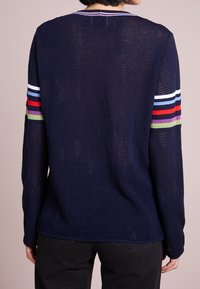 Granatowy sweter o teksturowanej powierzchni z okrągłym dekoltem, zdobiony wielokolorowymi paskami na rękawach w kolorach czerwonym, białym, zielonym i fioletowym.
