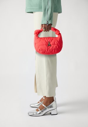 Red quilted handbag with a structured handle and a silver insect charm. Worn with beige straight-leg trousers and metallic silver heels.
