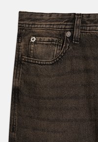 Černé džíny z denimu s detailním pohledem, obsahující přední kapsu, kovové nýty a texturovaný povrch. Klasický design s pěti kapsami.