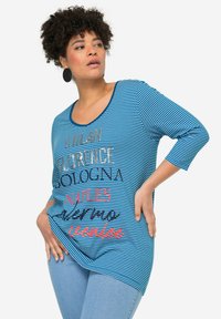 Blauwe en witte gestreepte T-shirt met een ronde halslijn en driekwart mouwen; heeft opvallende tekst in verschillende lettertypen en kleuren.