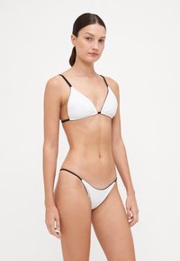 Ensemble bikini blanc comprenant un haut triangulaire avec des accents noirs et des fines bretelles, associé à un slip taille basse. Texture lisse, design minimal.