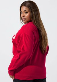 Sudadera roja de manga larga, con un diseño gráfico en la parte frontal. Tela suave con un corte relajado y puños y dobladillo acanalados.