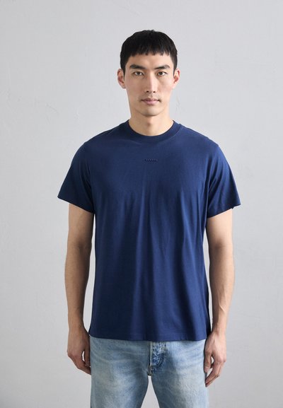 T-shirt en coton bleu marine à manches courtes, col rond, avec un petit logo imprimé au centre. Coupe régulière et texture douce.