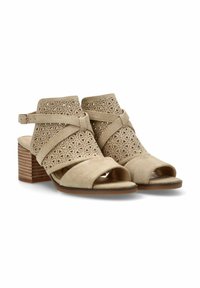 Sandalias de tobillo color beige con tira, hechas de ante, con un diseño floral recortado. Punta de los pies abierta y tacón bloque apilado. Textura suave y forma curvada.
