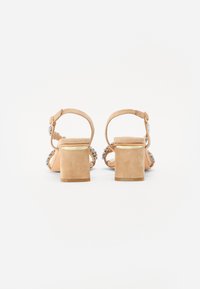 Beige semskede blokkhæl sandaler med ankelrem, pyntet med flerfarvede rhinsten og en glat mat overflade på hælen.
