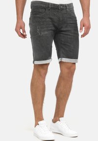 Shorts en denim gris avec revers retroussés, présentant une légère usure, des poches avant et une coupe décontractée, associés à des baskets blanches.