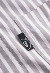 Gray and white striped fabric with a smooth texture. Features a stitched hem and a black branded label with white logo detail.