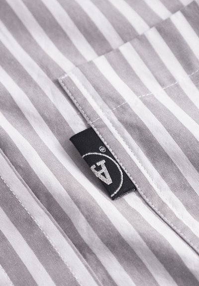 Grau und weiß gestreifter Stoff mit glatter Textur. Verfügt über einen genähten Saum und ein schwarzes Markenlabel mit weißen Logodetails.