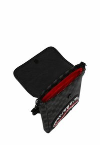 Borsa crossbody a scacchi nera con pattina aperta, fodera interna rossa e design di bocca di squalo sulla parte anteriore.