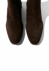 Botas de tobillo de ante marrón con punta afilada, textura suave y costuras mínimas. Diseño elegante y aerodinámico con un perfil bajo.