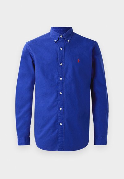 Langermet blå skjorte laget av bomull, med krage med knapper, frontknapper og en liten rød logo på brystet.