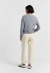 Grijze gebreide trui met ronde halslijn, geribbelde boorden en een hartlogo op de achterkant. Gecombineerd met crèmekleurige wijde broek en sneakers.