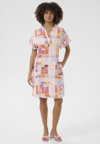 Korte mouw, kleed tot de knie in een patroon van pastel vierkanten. Heeft een v-hals, gerimpelde mouwen en een ontspannen pasvorm.