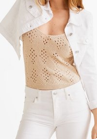 Top de tanque de punto beige con patrón abierto, combinado con una chaqueta de mezclilla blanca corta. El conjunto cuenta con jeans blancos de tiro alto.