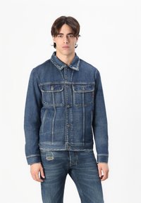 Denim jacket in dark blue with a button-up front, two chest pockets, and contrasting stitching. Raw hem and structured collar design.