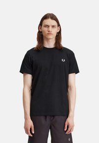 Camiseta de algodón negra con cuello redondo, mangas cortas y un pequeño logotipo blanco en el lado izquierdo del pecho. Textura suave, ajuste clásico.