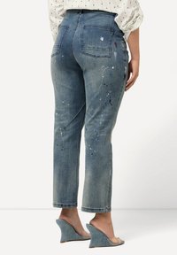 Modré denimové džíny se slim fit, zdobené bíle, modře a červeně stříkaným barvami. Džíny mají zadní kapsy a jsou zkrácené nad kotníkem.