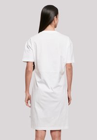 Weißes Baumwoll-T-Shirt-Kleid mit kurzen Ärmeln, lockerer Passform und einer Länge unterhalb des Knies. Mit einem grünen Etikett an der unteren Seite.