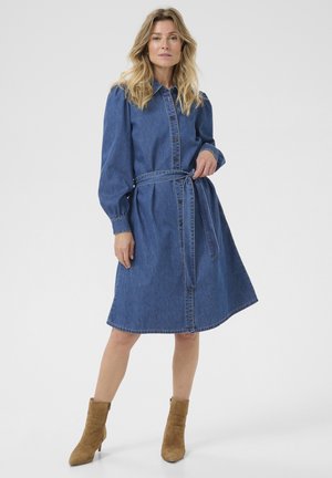 Denim dress, blue, with button front, long puff sleeves, and belted waist. Soft texture and knee-length hem. Worn with tan ankle boots.