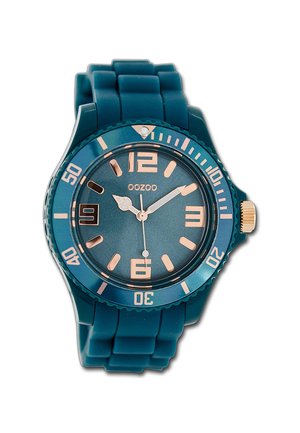 Montre en silicone teal avec un cadran rond, des accents en or rose, des marquages numériques audacieux et une lunette texturée. Comprend une fenêtre de date à 6 heures.