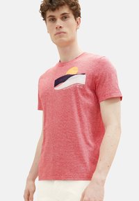 Rot gestreiftes Kurzarm-T-Shirt aus Baumwolle mit einer Tasche, die eine Stickerei mit Sonne und Welle zeigt. Runder Halsausschnitt.