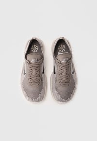 Grå Nike Free sneakers med en overdækkende mesh, teksturerede mønstre, flade snørebånd og en polstret tunge. Sort Swoosh-logo på siderne.
