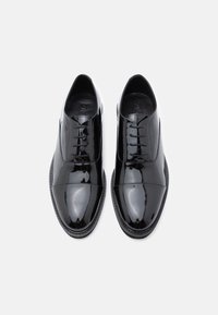 Sorte lakksko i skinn med rund tå, snøring og en glatt, blank finish. Har en diskret detalj på tuppen.