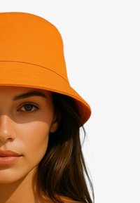 Cappello a secchiello arancione in tessuto morbido, con ampio bordo e design senza cuciture. La texture liscia completa l'aspetto contemporaneo.