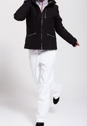 Chaqueta negra impermeable con bolsillos con cremallera y capucha ajustable, combinada con pantalones de nieve blancos y calzado negro, que muestran un diseño elegante.