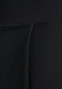 Gros plan sur un tissu noir avec une couture verticale créant un pli semblable à une poche sur le côté droit.