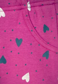 Roze stof met een patroon van teal en witte harten, met kleine teal stippen. De textuur is zacht, met zichtbare stikdetails.