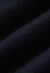 Ciemnoniebieska tkanina o teksturze z miękkim, puszystym wykończeniem, z złożonymi warstwami wykazującymi niewielkie różnice w głębokości i odcieniach.