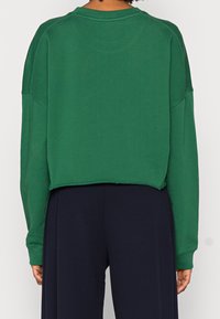 Zielony krótki sweatshirt z okrągłym dekoltem, opadającymi ramionami i surowym wykończeniem, wykonany z miękkiego, teksturowanego materiału.