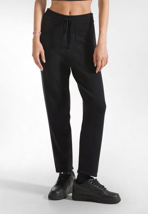 Zwarte, ontspannen sweatpants met een trekkoord in de taille, geribbelde textuur, taps toelopende vorm, gecombineerd met zwarte sneakers.