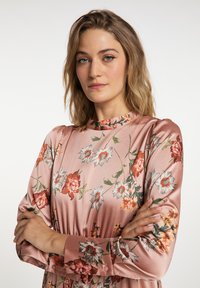 Rochie florală din satin roz, cu guler înalt, mâneci lungi și detalii cu nasturi. Prezintă diverse modele colorate de flori pe un fundal moale.