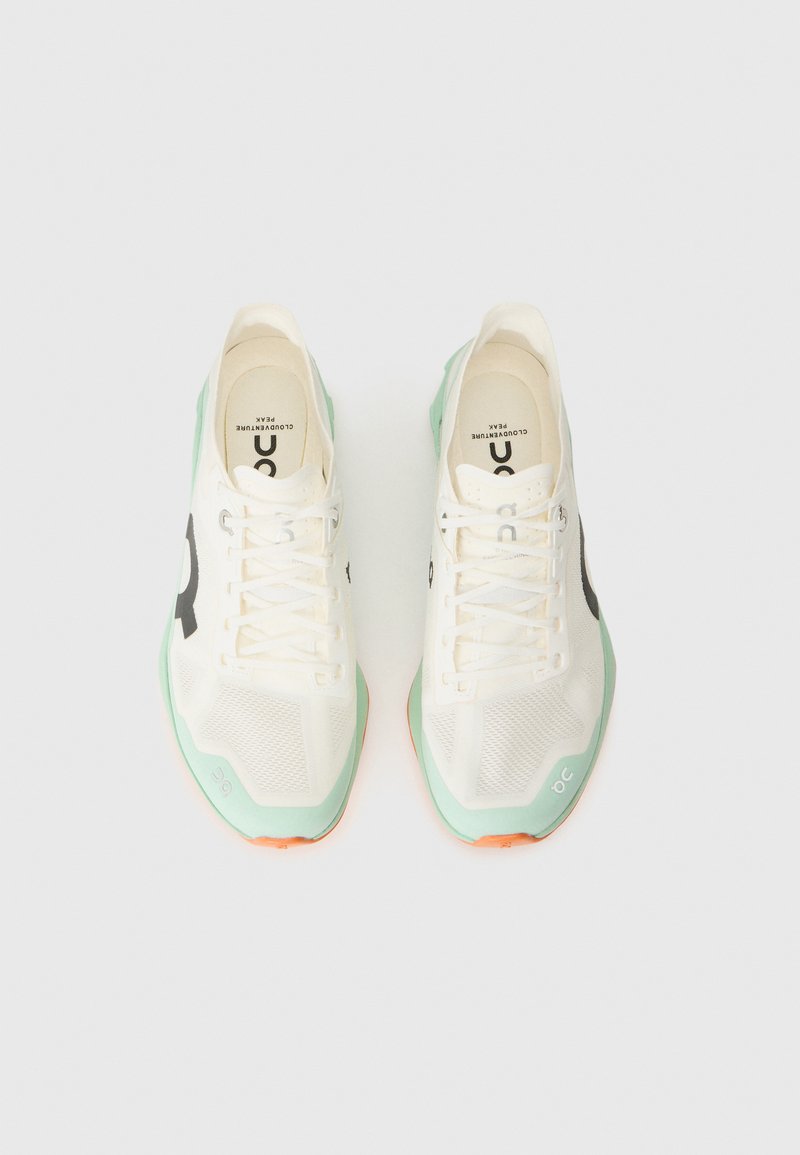 Zapatillas de running de malla blanca con suela verde menta y acentos naranjas. Cuenta con cordones y un gran logo negro en el lateral. Diseño texturizado único.