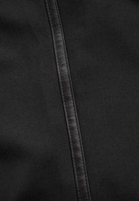 Detail čiernej látky zobrazujúci rovný vertikálny šev s dvojitým prešitím na textúrovanej ploche.