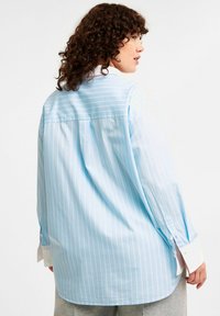 Ljusblå, randig skjorta med långa ärmar, knappmanschetter och en avslappnad passform. Har en vit krage och subtil textur.