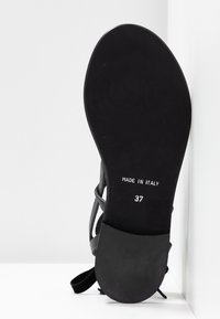 Semelle de sandale noire vue de face avec "Made in Italy" et taille 37 imprimés en blanc sur un fond blanc uni.