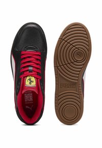 Chaussures de sport noires et rouges avec une tige en cuir lisse, un bout perforé, une semelle en caoutchouc et un détail de logo jaune sur la languette.