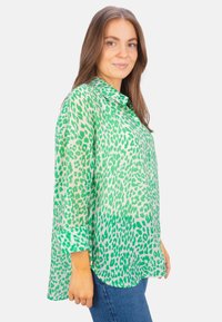 Green animal print shirt with a collar, long sleeves, and a loose fit. Lightweight fabric features a blend of dark and light green patterns.