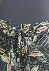 Kalhoty s opaskem na stahování, zdobené vícebarevným vzorem listí na tmavém pozadí, mají hladkou texturu a lehkou látku.