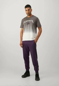 Γκρι και λευκό gradient μπλούζα με λογότυπο "FORTNITE", συνδυασμένη με μωβ παντελόνια φόρμας. Μαύρα παπούτσια ολοκληρώνουν την εμφάνιση.