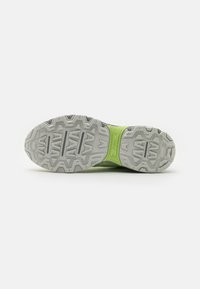 Semelle d’une chaussure de sport avec une bande de roulement texturée grise et une partie centrale verte, conçue pour l’adhérence et le soutien sur diverses surfaces.