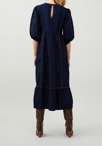 Dunkelblaues Baumwollkleid mit Puffärmeln, gestuftem Saum und kontrastierenden Ziernähten. Es hat eine kleine Schlüssellochöffnung auf der Rückseite.