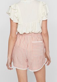 Blouse beige clair à volants avec dos transparent, associée à un short rayé rose et blanc avec une poche arrière et une bordure en dentelle le long de l'ourlet.